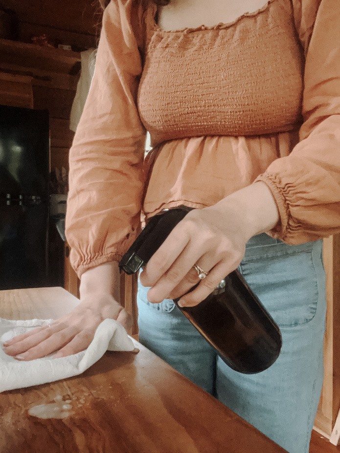 Caitlin wiping down a wooden counter with an amber glass spray bottle